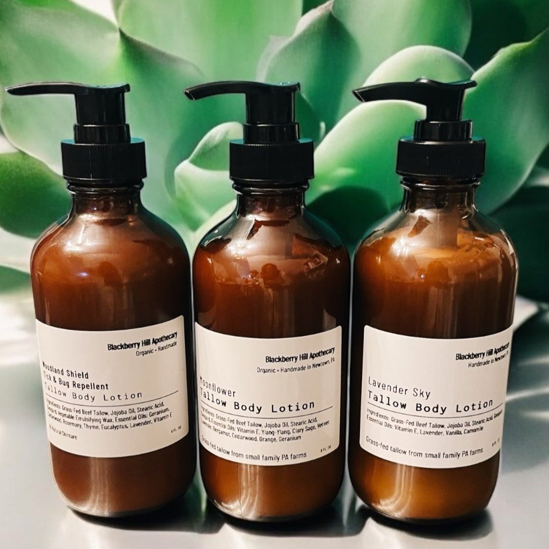 Three bottles of body lotion with pump dispensers on a reflective surface with green foliage in the background.