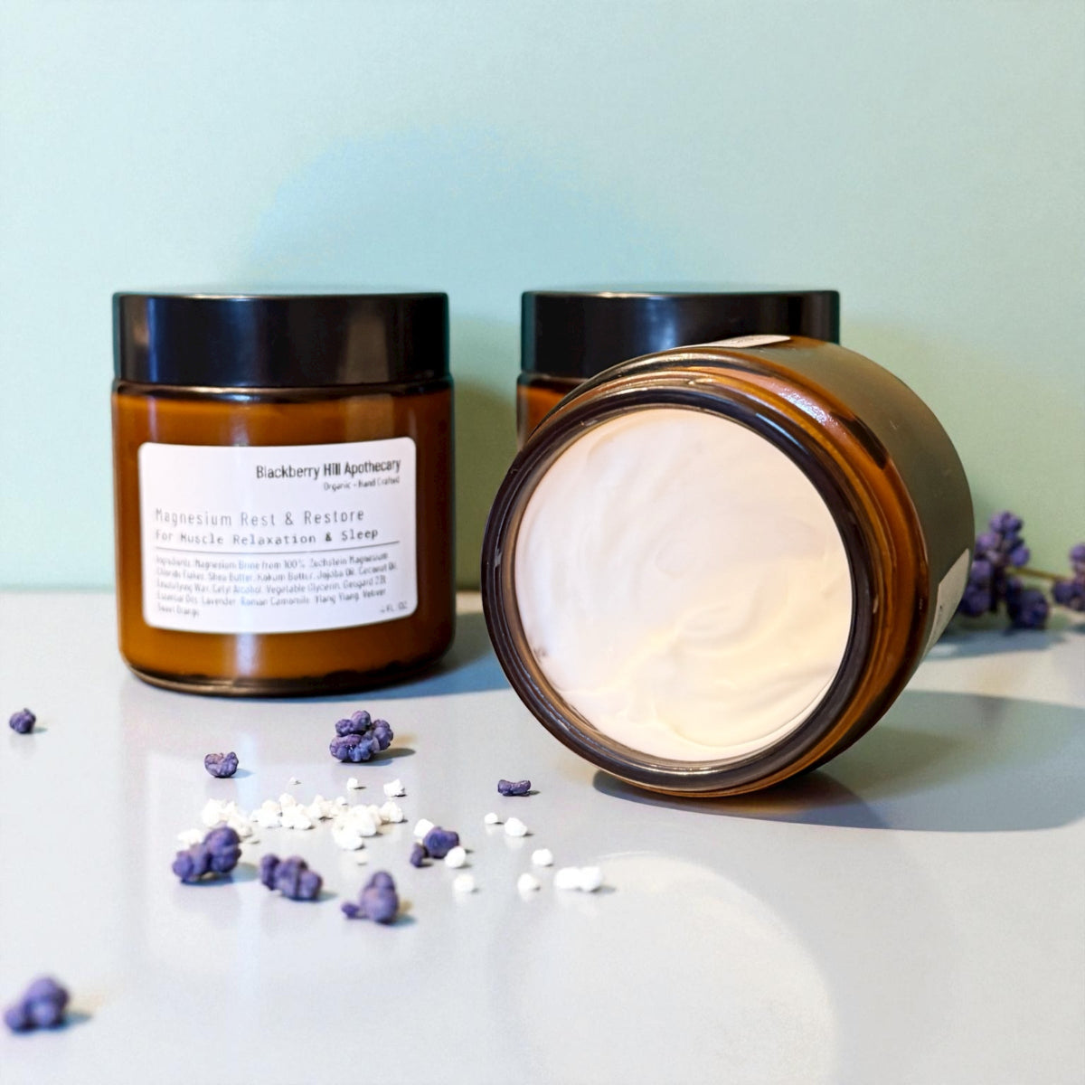 Two brown jars with black lids on a light surface with scattered purple flowers and white petals.