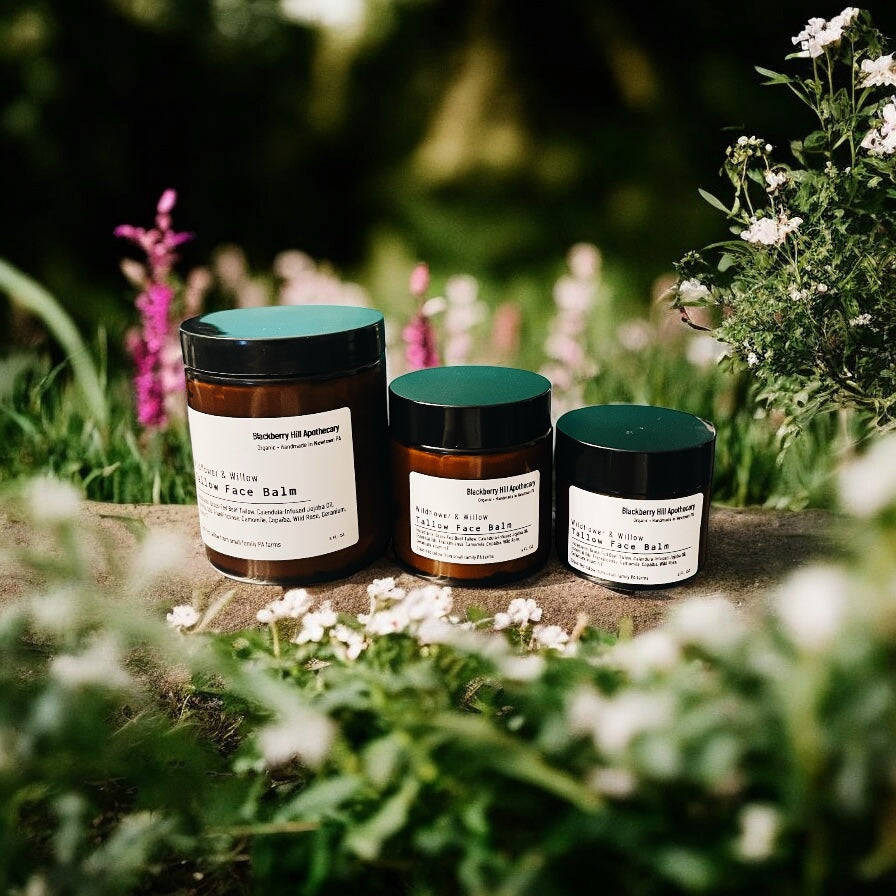Three jars of face balm on a stone surface with a natural, garden background.