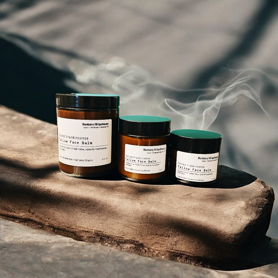 Three jars of face balm on a stone surface with smoke in the background