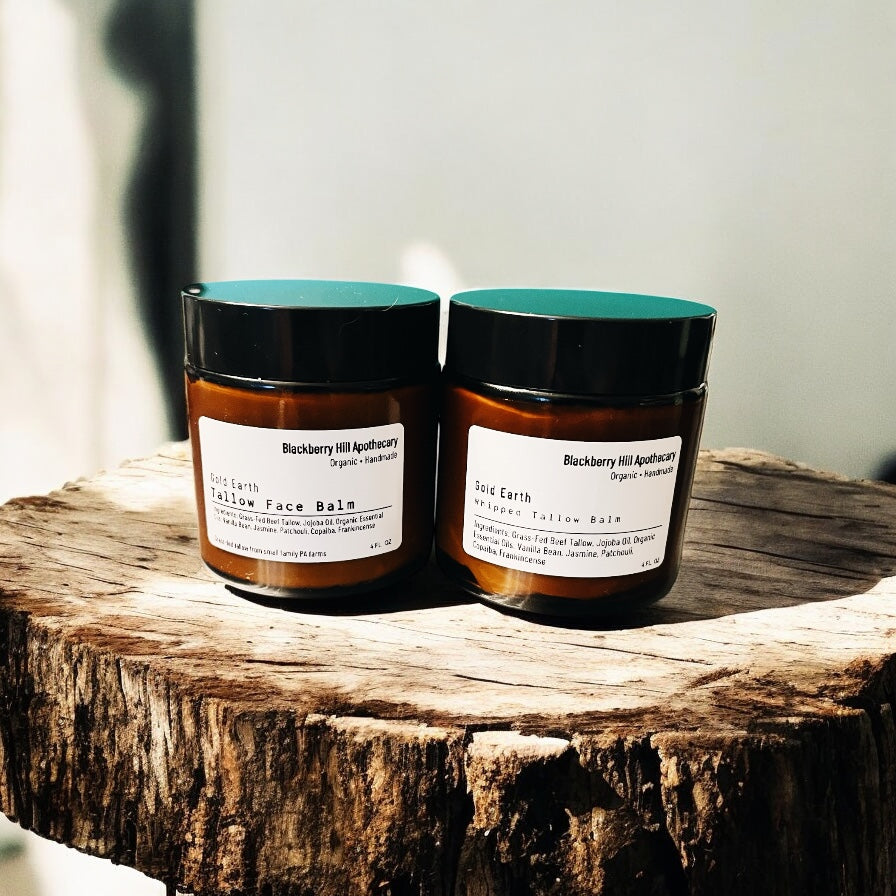 Two jars of 'Blackberry Hill Apothecary' balm on a wooden surface with a neutral background.