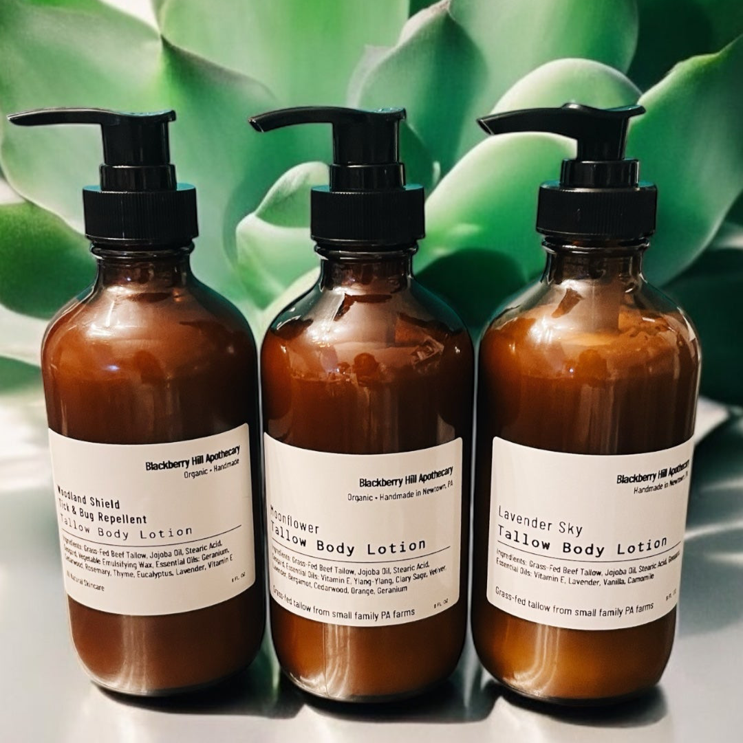 Three brown bottles of body lotion with pump dispensers on a reflective surface with green foliage in the background.