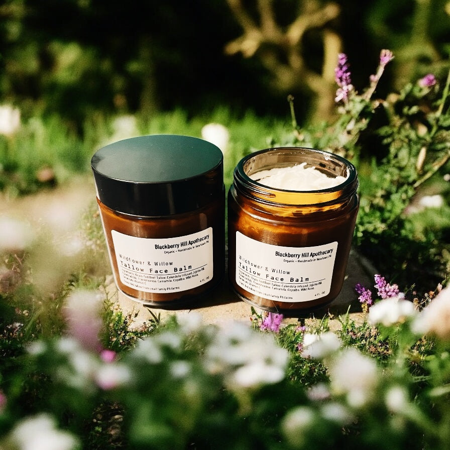 Two jars of 'Blackberry Hill Apothecary' balm on a natural background with flowers.