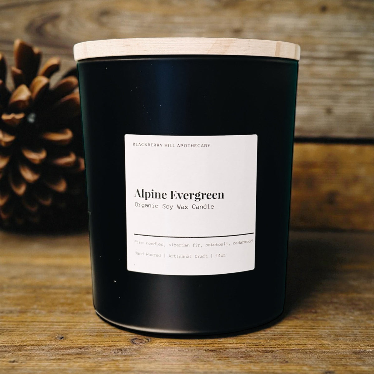 Black candle with a white label on a wooden surface, featuring the brand 'Blackberry Hill Apothecary'.