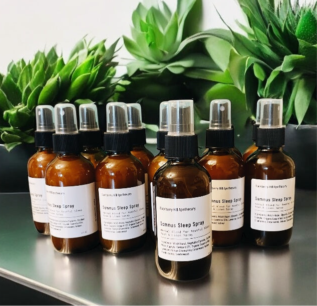 Row of amber glass bottles with black sprayers on a reflective surface with green plants in the background