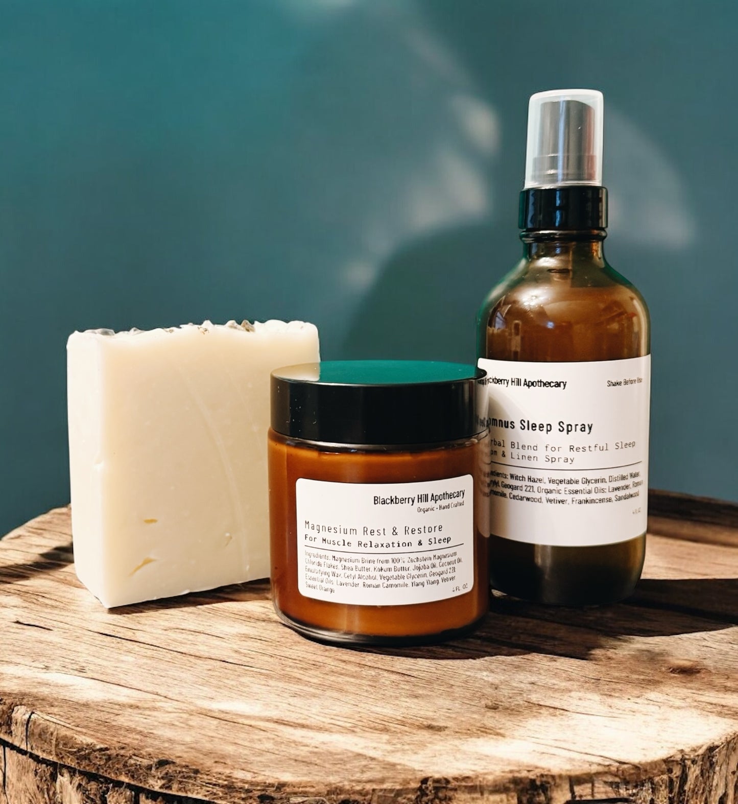 Three natural products including a bar of soap, a jar, and a spray bottle on a wooden surface with a blurred green background.